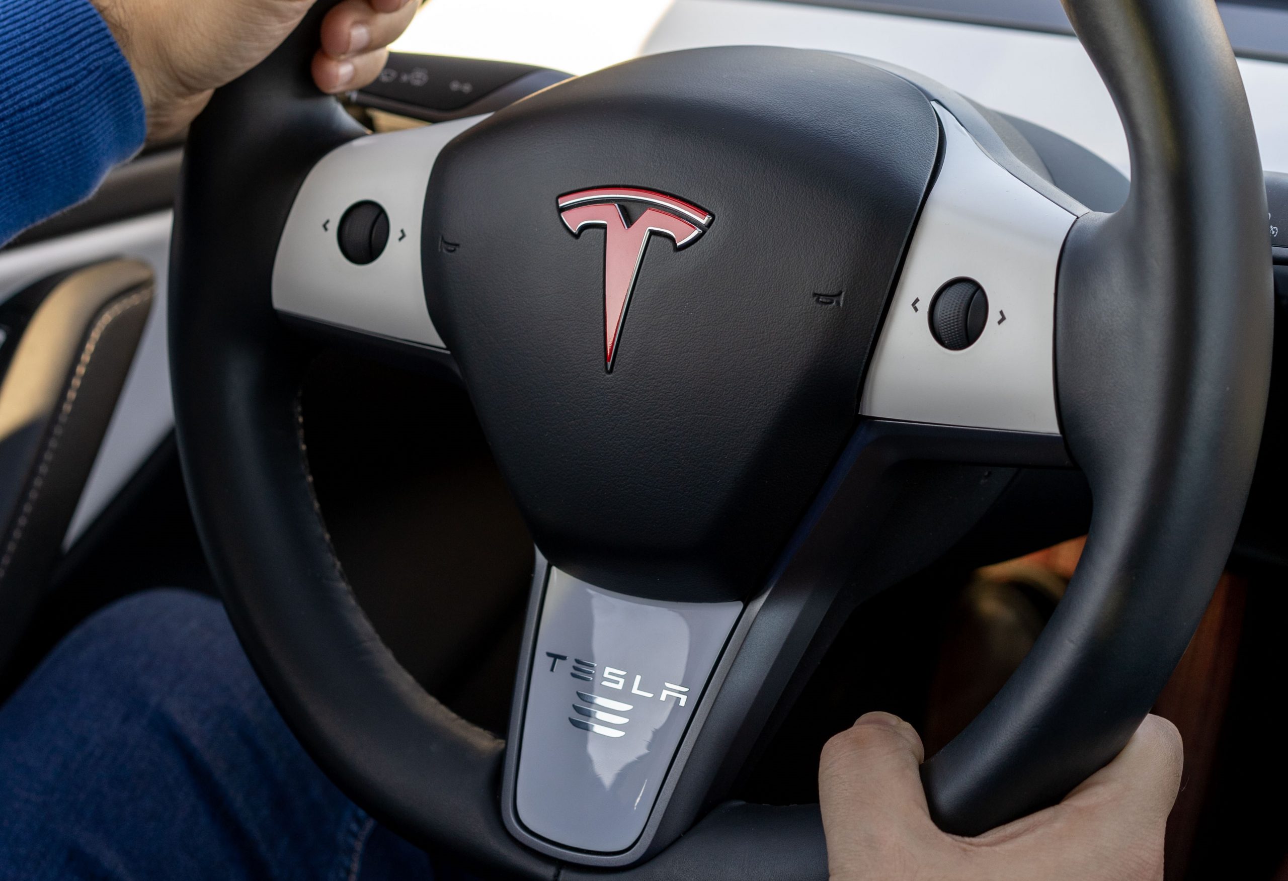 Murcia, Spain - DECEMBER 1, 2019: Young man is driving a Tesla car and is holding the steering wheel. The insignia of Tesla on the wheel of the plug-in electric car Model 3, a mid-size / compact executive luxury four-door sedan manufactured and sold by Tesla, Inc.
